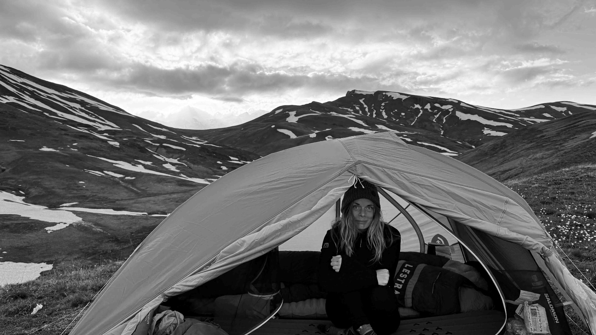 Marine assise dans une tente face aux montagnes enneigées, en noir et blanc