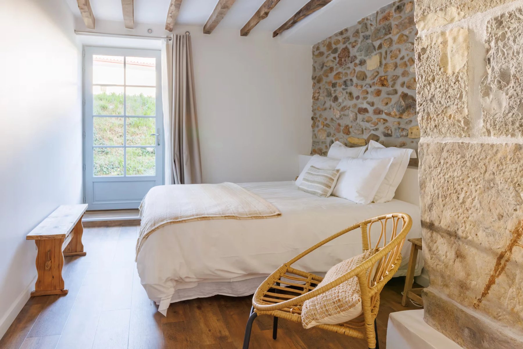 Chambre avec mur en pierre apparente, poutres et lit en lin blanc