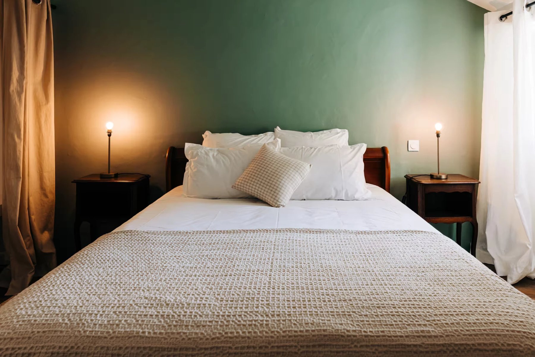 Chambre calme dans l'ancien fenil basque, linge blanc et coussins verts, chevet en bois sombre