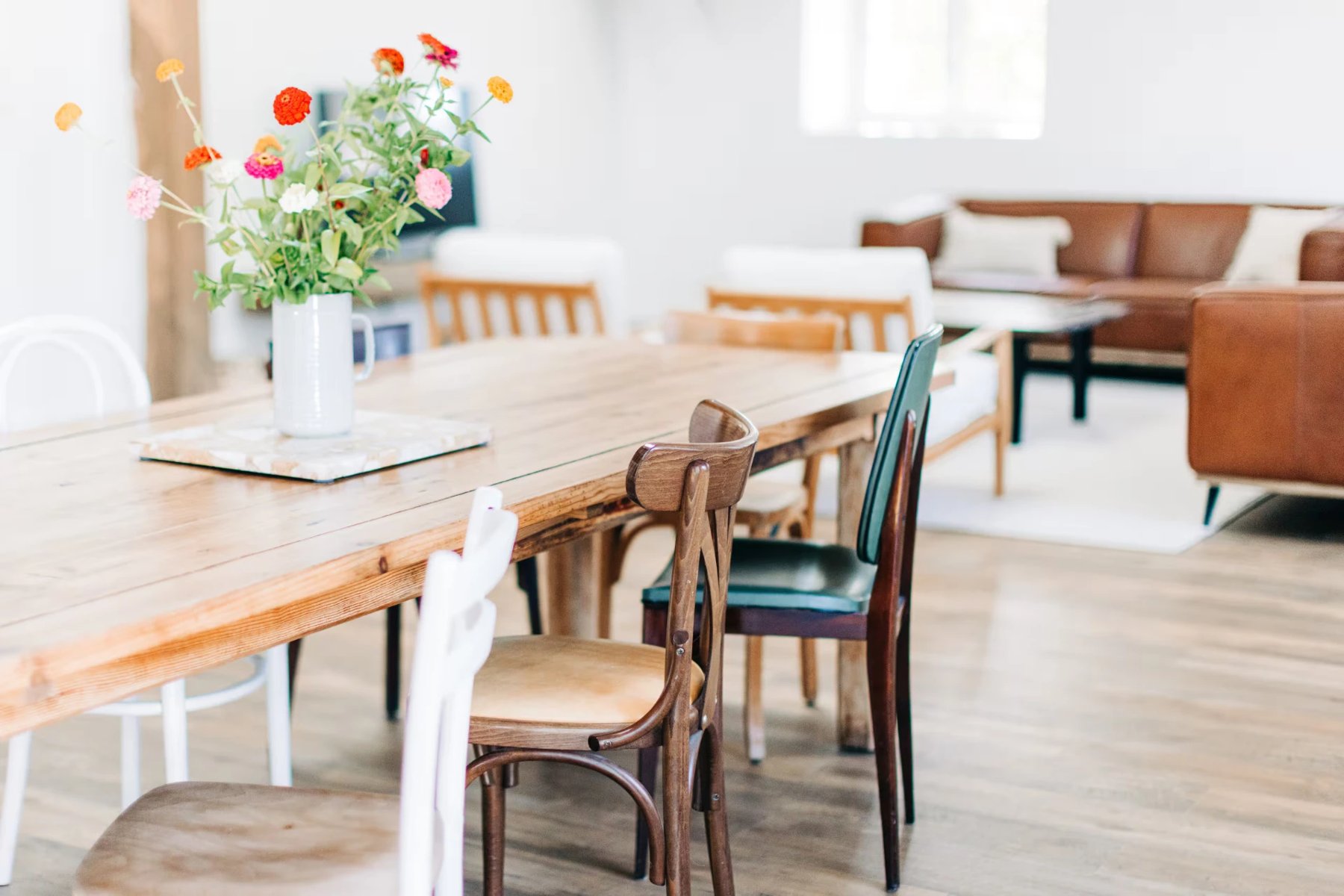 Grande table commune en bois avec bouquet de fleurs, ouverte sur le salon
